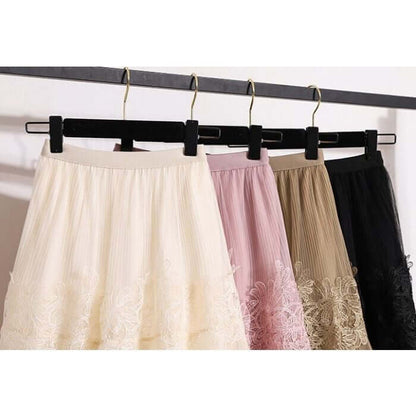 Four stylish lace and tulle midi skirts in cream, pink, gray, and black hanging elegantly on a black rack.